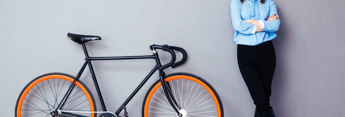 Cheerful young businesswoman standing near bicycle