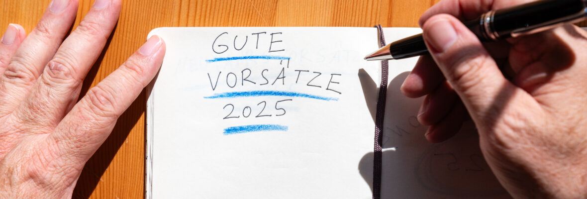 Die Hände eines Mannes Menschen schreiben in ein Notizbuch, seine guten Vorsätze für das neue Jahr 2025 auf einem Holztisch mit einem Stift